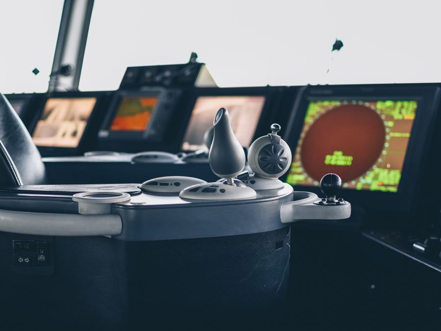 A ship's bridge console with azimuth controls, radar and chart displays lit across the consoles