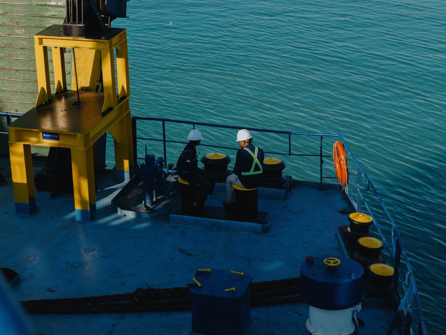Two seafarers in hard hats working on the mooring deck of a cargo ship at sea